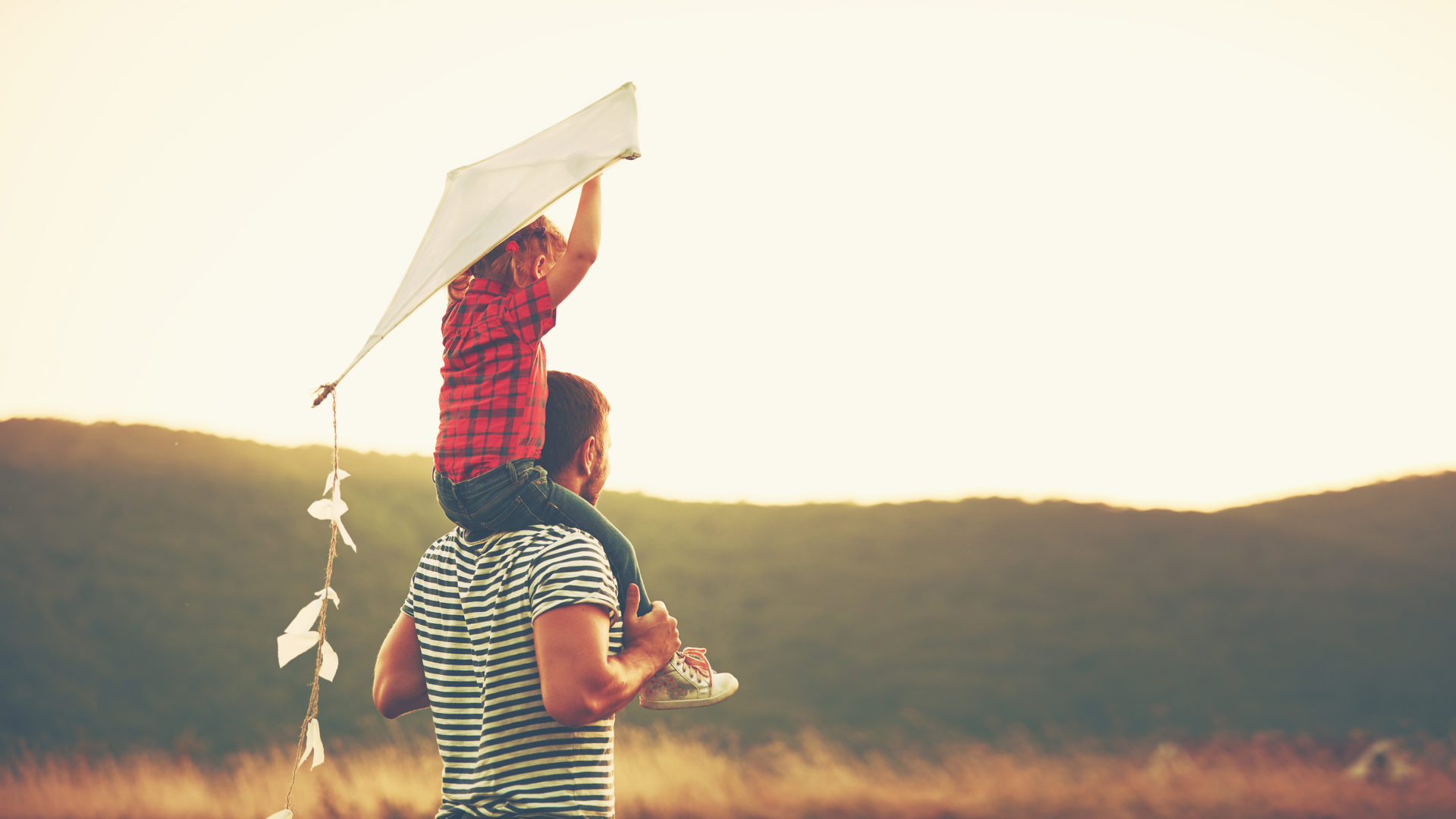 Dad with little girl on his shoulders flying a kite.